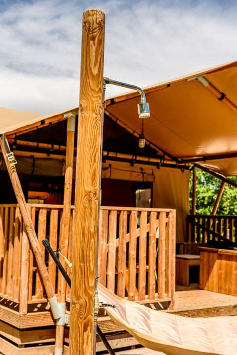 Outdoor shower and hammock in front of a safari tent at Dune Agriturismo in Italy on a sunny day.