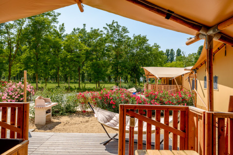 Vista dal patio di una tenda safari al Dune Agriturismo in Italia, circondata da fiori e alberi verdi.