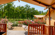 Vue depuis la terrasse d'une tente safari au Dune Agriturismo en Italie, entourée de fleurs et d’arbres verts.