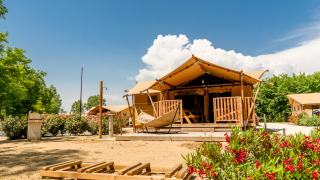 Tenda safari con veranda, amaca, servizi igienici e aria condizionata sotto un cielo soleggiato.