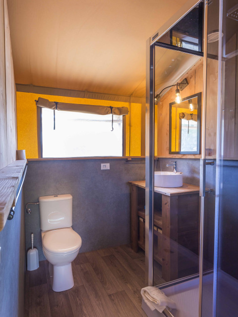 Badezimmer im Safari-Zelt von Dune Agriturismo in Italien mit Toilette, Dusche und Holzmöbeln.