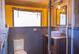 Bagno in una tenda safari al Dune Agriturismo, Italia, con WC, doccia e mobile lavabo in legno.