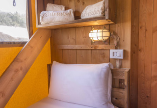Interno tenda Safari presso Dune Agriturismo, Italia, con letto in legno, mensole e lampada rustica.