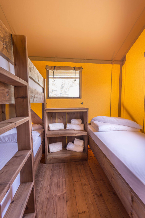 Indersiden af et safari telt på Dune Agriturismo i Italien med køjeseng, enkeltseng og træmøbler.
