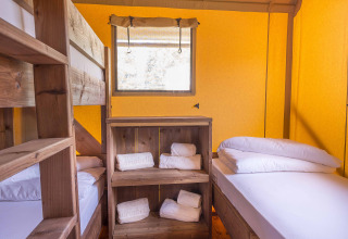 Interior of a safari tent at Dune Agriturismo in Italy with bunk bed, single bed, and wooden furniture.