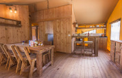 Interior of a safari tent at Dune Agriturismo in Italy featuring wooden furniture and a cozy kitchen area.