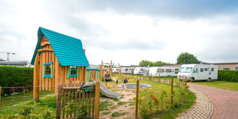 Parco giochi dell’Holiday Village Knokke con casetta colorata, bambini, roulotte e area verde.