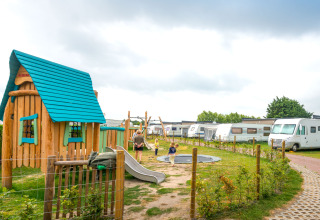 Aire de jeux à Holiday Village Knokke avec maisonnette colorée, enfants, caravanes et pelouse verte.