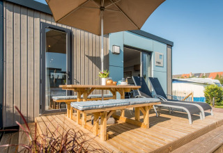 Zonnig terras met houten picknicktafel, banken en ligstoelen bij Holiday Village Knokke in België.