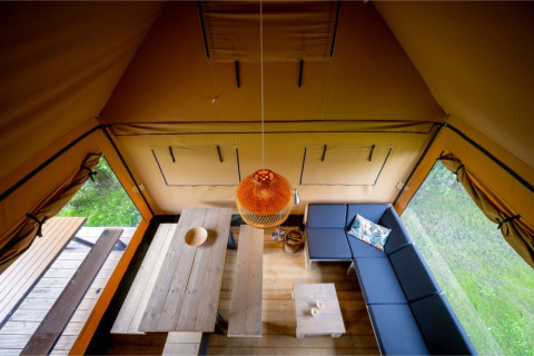 Vue de l’intérieur de la tente safari Nomad Family avec canapé, table à manger et coin salon à Knokke, Belgique.