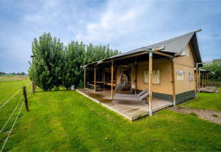 Safaritent 'Nomad Family' bij Holiday Village Knokke, België, met houten veranda en groene omgeving.
