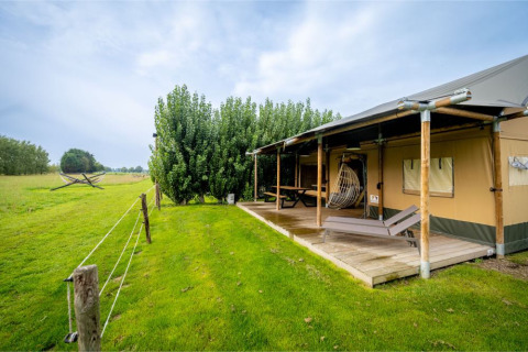 Safaritent 'Nomad Family' op Holiday Village Knokke, België, met houten veranda, ligstoelen en groen grasveld.