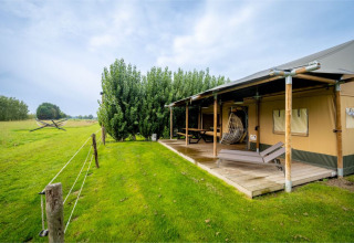 Safaritent 'Nomad Family' op Holiday Village Knokke, België, met houten veranda, ligstoelen en groen grasveld.