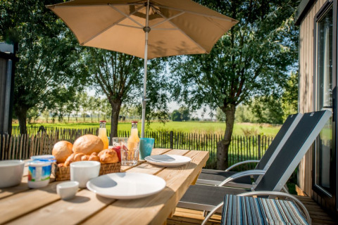 Outdoor breakfast on terrace at Holiday Village Knokke with parasol and view of green fields in Belgium.