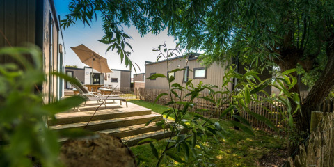 Terrazza con lettini e ombrellone al Holiday Village Knokke, Belgio, circondata da alberi e casette.