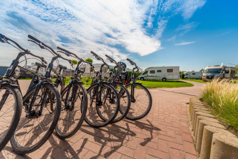 Bicicletas de alquiler listas en Holiday Village Knokke, con autocaravanas y cielo azul de fondo.