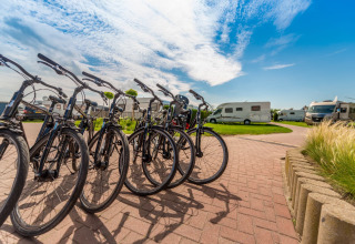 Leihfahrräder auf dem Gelände des Holiday Village Knokke, umgeben von Wohnmobilen und blauem Himmel.