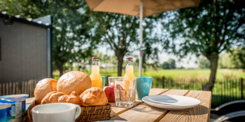 Buiten ontbijten met broodjes, croissants en sap op een houten tafel in Holiday Village Knokke, België.