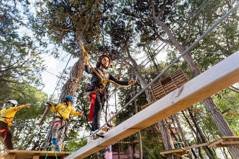 Bambini con caschi e imbragature percorrono un percorso avventura sugli alberi al campeggio Spina Family Collection.