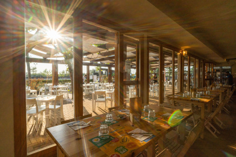 Sunny dining area at Spina Family Collection campsite in Emilia-Romagna, Italy, with indoor and outdoor seating.