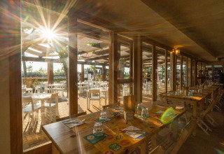 Zona pranzo soleggiata al campeggio Spina Family Collection in Emilia-Romagna, Italia, con tavoli dentro e fuori.