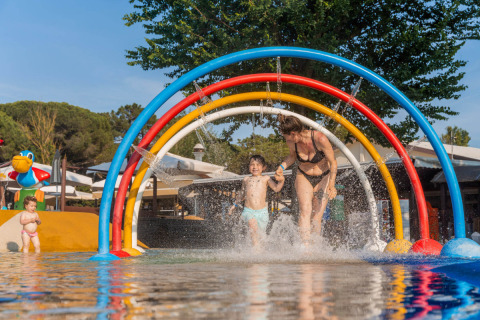 Family enjoys water play under colorful arches at Spina Family Collection campsite in Emilia-Romagna, Italy.