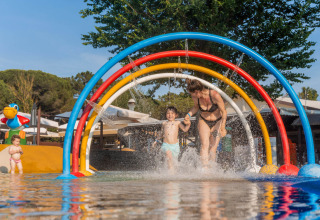 Family enjoys water play under colorful arches at Spina Family Collection campsite in Emilia-Romagna, Italy.