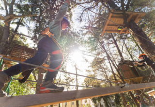 Bambini con imbracatura su un ponte di legno al parco avventura Spina Family Collection in Italia.