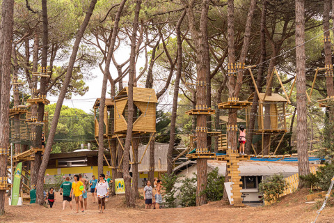 Bambini e adulti si divertono in un percorso avventura tra gli alberi con casette di legno in un campeggio familiare.