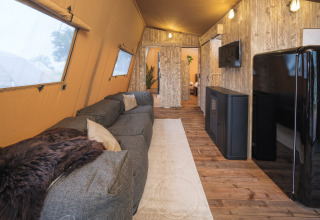Interior view of a Tribe lodgetent at Holiday park Mölke, Netherlands, featuring couch, rug, and TV.