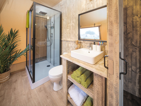 Moderne badeværelse i Tribe lodgetelt på Holiday park Mölke, Holland, med bruser, håndvask og grønne håndklæder.