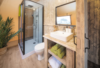 Moderne badeværelse i Tribe lodgetelt på Holiday park Mölke, Holland, med bruser, håndvask og grønne håndklæder.