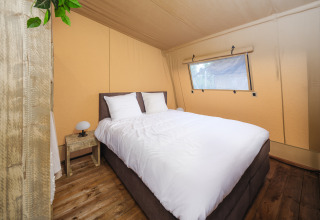 Soveværelse i en Tribe lodgetent med dobbeltseng, træbord og vindue i Holiday park Mölke, Holland.