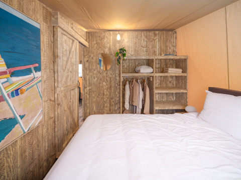 Bedroom inside a Tribe lodgetent at Holiday park Mölke, Netherlands, with rustic bed and wooden closet.