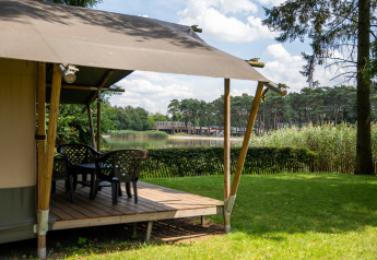 Safari-Zelt mit Terrasse am See im Family Park Goolderheide, Belgien, umgeben von Natur und Bäumen.