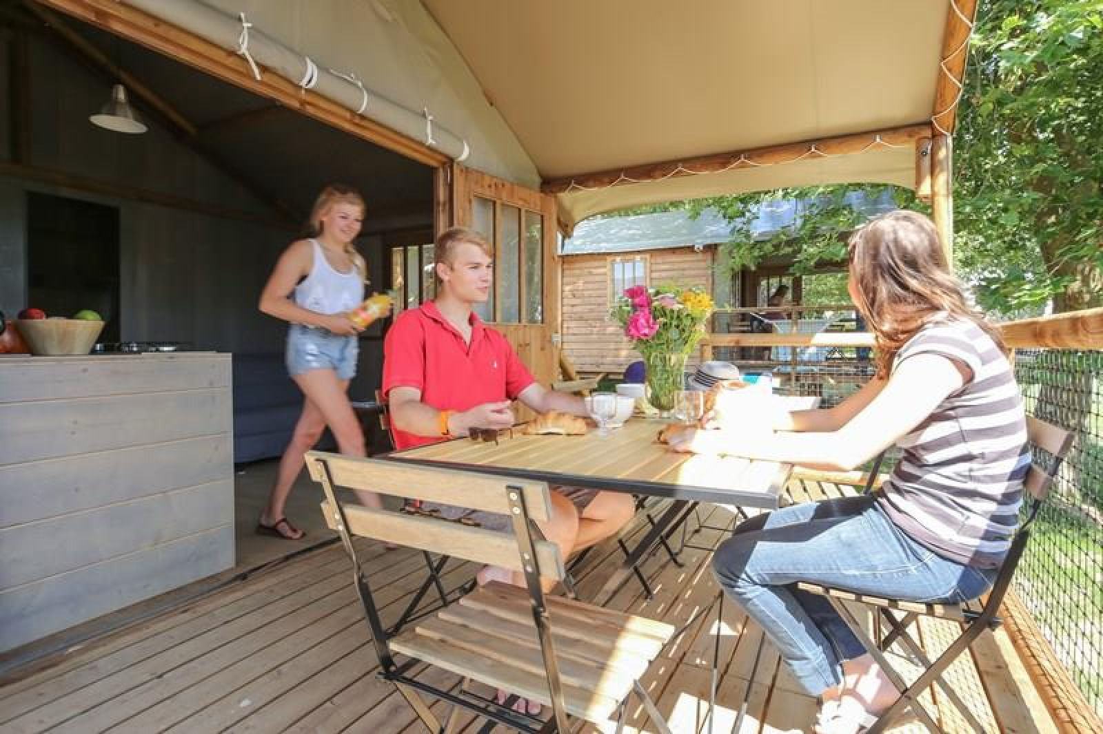 Drie personen genieten van een maaltijd op het terras van Hut Lodge COMFORT bij Flower Camping Le Conleau.