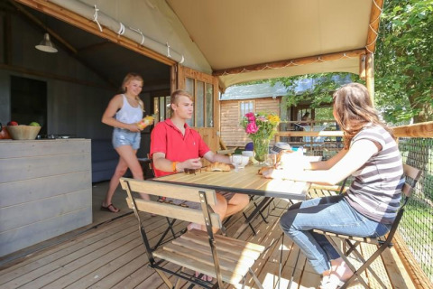 Three people enjoying a meal on the terrace of Hut Lodge COMFORT at Flower Camping Le Conleau, France.