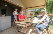 Three people enjoying a meal on the terrace of Hut Lodge COMFORT at Flower Camping Le Conleau, France.