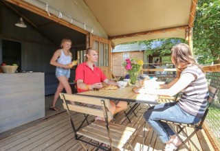 Three people enjoying a meal on the terrace of Hut Lodge COMFORT at Flower Camping Le Conleau, France.