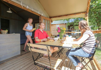Tre personer nyder et måltid på terrassen i Hut Lodge COMFORT ved Flower Camping Le Conleau, Frankrig.