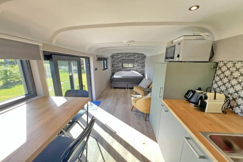 Vista interior de Pine Tree Tiny Cottage en Bélgica con cocina, mesa de comedor y cama al fondo.