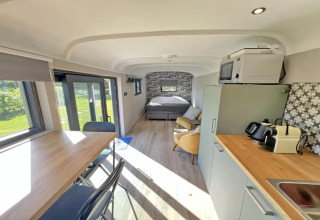 Vista interior de Pine Tree Tiny Cottage en Bélgica con cocina, mesa de comedor y cama al fondo.