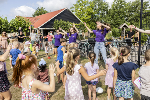 Niños bailan y juegan al aire libre junto a una tienda safari en el camping 't Veld en los Países Bajos.