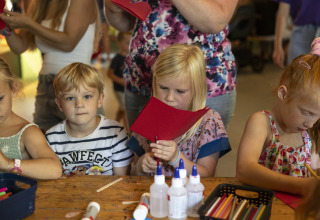 Children enjoying arts and crafts with paper and glue at a table during a glamping accommodation stay.