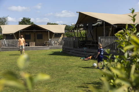 Padre e hijo juegan fútbol frente a una tienda safari de lujo en el camping 't Veld en Países Bajos.