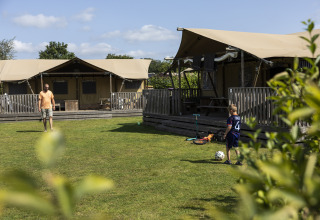 Padre e hijo juegan fútbol frente a una tienda safari de lujo en el camping 't Veld en Países Bajos.