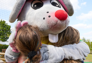Dos niños abrazan una gran mascota de ratón con gorra roja en la Safari tent «de luxe» del Camping 't Veld, Países Bajos.