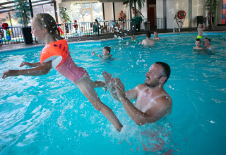 Un hombre juega con una niña en una piscina cubierta del Safari tent de luxe en el Camping 't Veld, Países Bajos.
