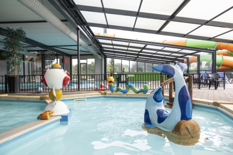 Piscina cubierta con juguetes acuáticos y toboganes en un alojamiento de glamping ideal para familias.