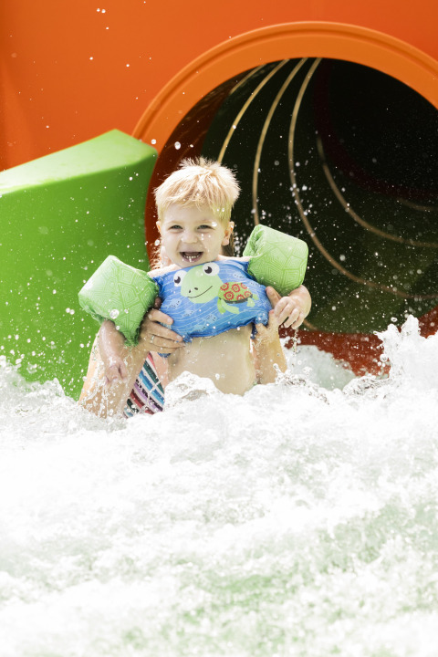 Un niño sonriente con flotadores sale de un tobogán de agua en Beach chalet del Camping 't Veld en los Países Bajos.